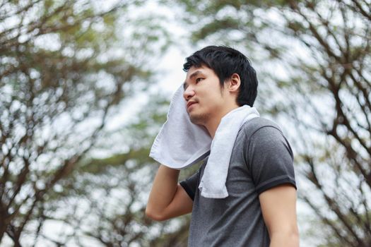 young sporty man resting and wiping his sweat with a towel after workout sport exercises outdoors at the park