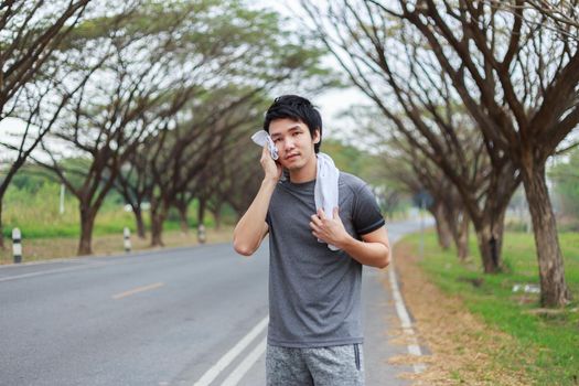 young sporty man resting and wiping his sweat with a towel after workout sport exercises outdoors at the park