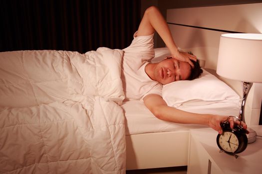 unhappy man being awakened by an alarm clock in his bedroom in the morning