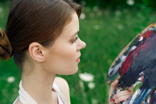 Woman in white dress with palette of paints on nature art drawing. High quality photo