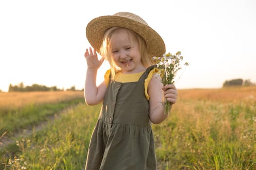 A little blonde girl in a straw hat walks in a field with a bouquet of daisies. The concept of walking in nature, freedom and an eco-friendly lifestyle.