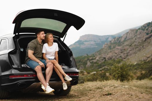 Young happy couple on a road trip sitting in car trunk outdoor