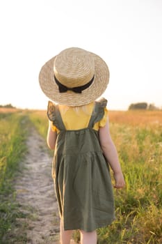 A little blonde girl in a straw hat walks in a field with a bouquet of daisies. The concept of walking in nature, freedom and an eco-friendly lifestyle.