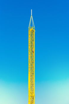 Attraction yellow tower in an amusement park against a blue sky background.