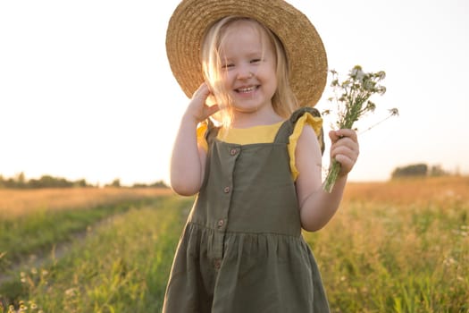 A little blonde girl in a straw hat walks in a field with a bouquet of daisies. The concept of walking in nature, freedom and an eco-friendly lifestyle.
