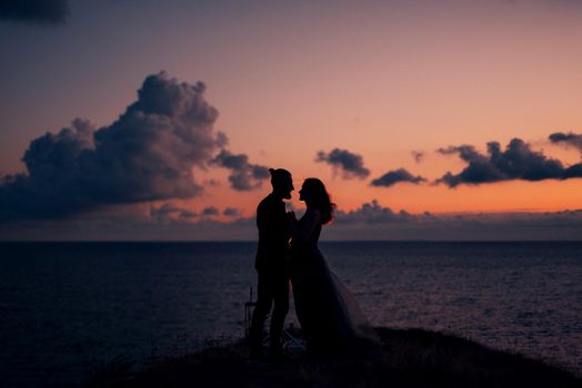 silhouettes of a happy young couple guy and girl on a background of orange sunset in the ocean