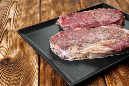 Two raw beef steaks on dark wooden table, close up