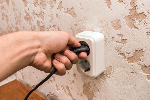 A man hand inserts or removes a plug from an outlet in a modern interior. Safe use of electrical appliances concept.