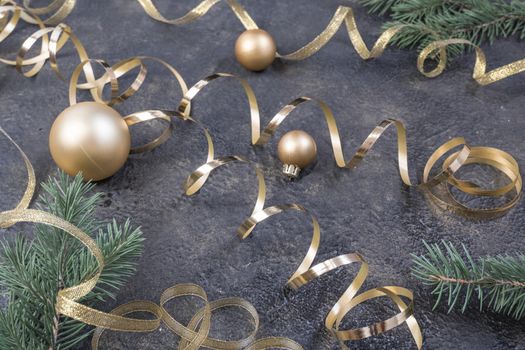 Christmas composition of yellow Christmas balls, fir branches and a gold ribbon on a black with gold embossed background