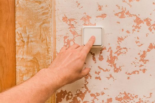 The guy's hand turns off the light with an electric switch in a modern room interior background.