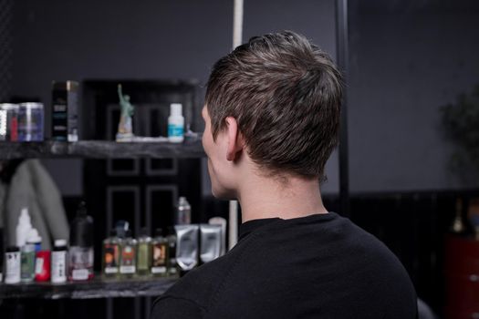 Portrait occiput of a guy of Caucasian appearance with dark hair in a black sweatshirt against the background of a hairdresser. The need for hairdressing services and cutting overgrown hair.