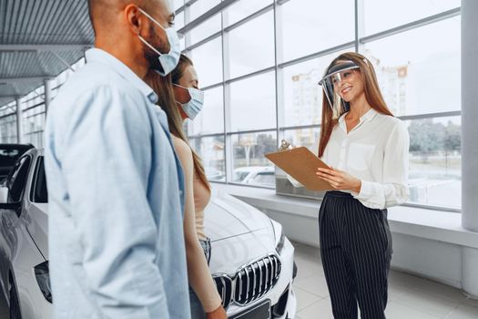 Woman car dealer consulting buyers wearing medical face shield. Coronavirus job requirements concept