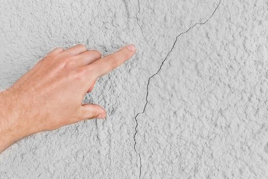 Male construction worker hand points cracks on white wall background. Renovation concept.