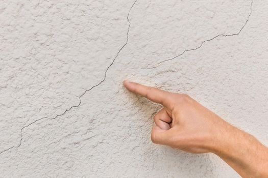 Male construction worker hand points cracks on white broken wall background. Renovation or repair concept.