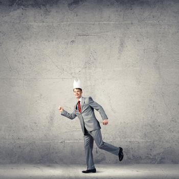 Young handsome businessman wearing white paper crown running in a hurry