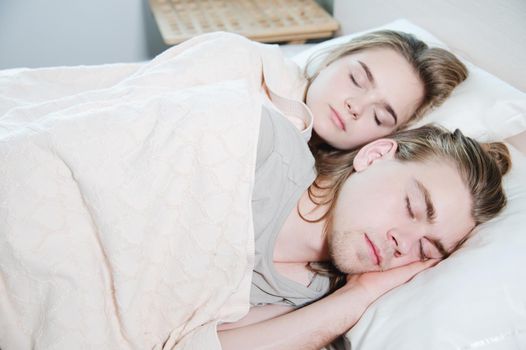 Close-up of a young couple in bed sleeping in an embrace, hiding behind a blanket. The concept of a young family and healthy sleep.