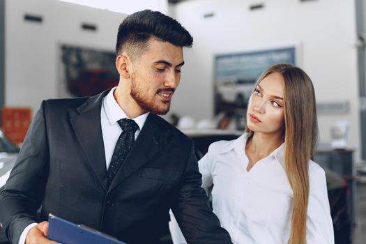 Man car dealer showing a woman buyer a new car in car salon