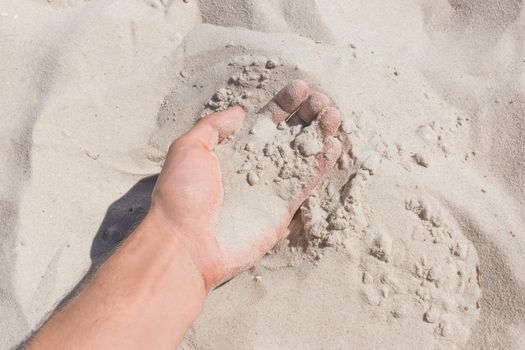 The guy's hand takes or touches the white beach sand close up.