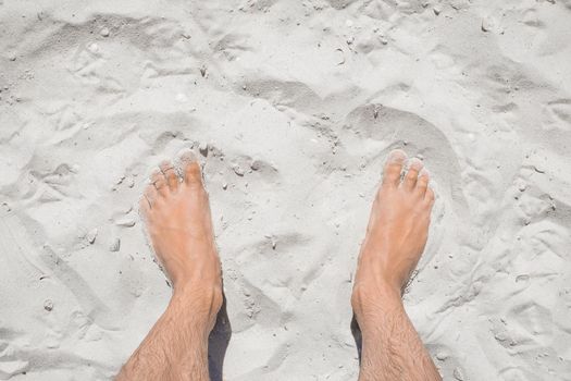 The young man's legs stand relaxed on the white beach sand, the view from above.