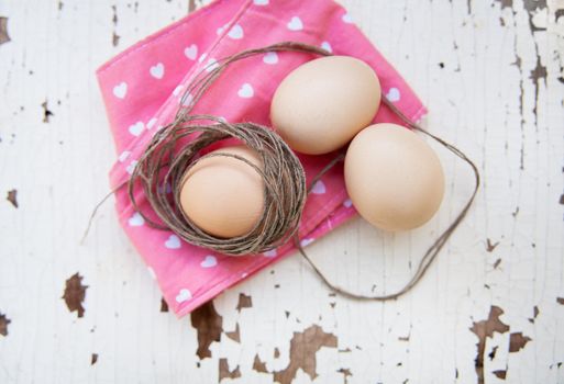 Eggs on pink tablecloth and old rope over vintage cracky white wooden background. Top view