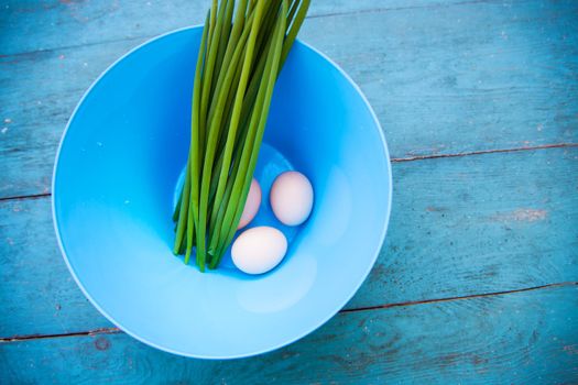 Natural white eggs in a blue bowl and Spring onions over old blue wooden table. Top view