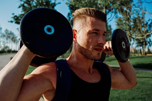 athletic man with dumbbells in his hands in the park training lifestyle. High quality photo