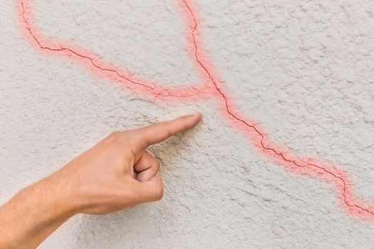 Male construction worker hand points cracks on white broken wall background. Renovation concept.