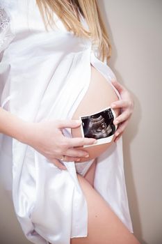 Close up of pregnant woman holding ultrasound scan on her tummy