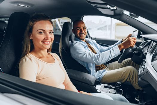 Joyful young couple looking around inside a new car they are going to buy in a car shop dealership