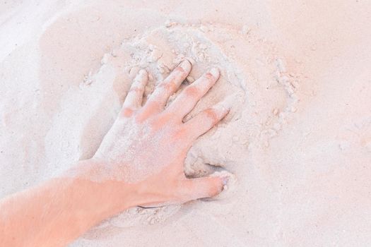 The guy's hand takes or touches the white beach sand close up.