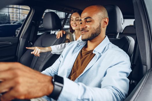 Young attractive caucasian woman salesperson in car showroom showing a car to her male African American client