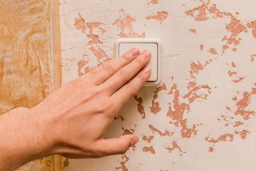 The man's hand turns off the light with an electric switch in a modern room interior background.