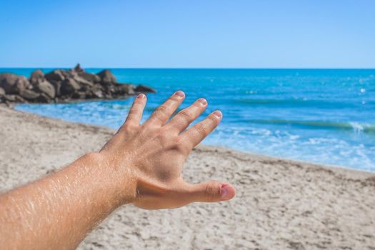 The young man stretched his hand forward to the sea and sky on the beach. The concept of freedom and rest at sea.