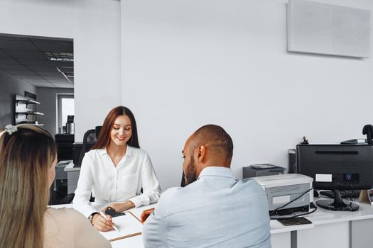 Young woman car seller showing contract to couple of car buyers in her office