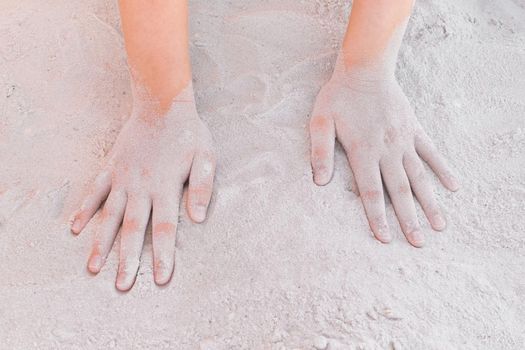 The hands of a young girl lie on a warm white beach sand background.
