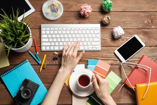 Woman designer typing on keyboard. Creative workspace with color swatches, colorful pencils and cup of coffee. Professional product designing. Coloristics and product branding in visual design studio