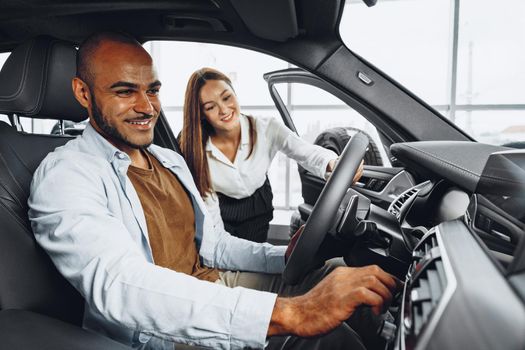 Young attractive caucasian woman salesperson in car showroom showing a car to her male African American client