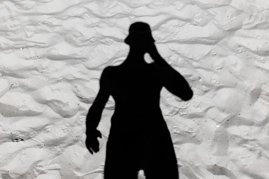 Black male silhouette shadow on white beach sand background.