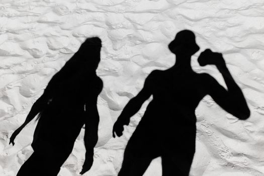 Dark black silhouette of a guy and a girl shade on a white beach sand background.