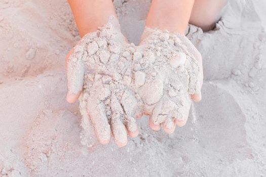 The hands of a young girl hold a pile of white sand close-up.
