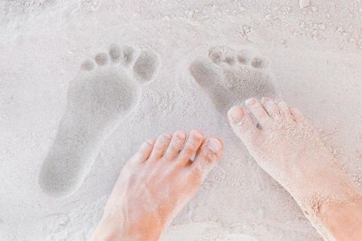 Traces of male and female legs on white beach sand background close-up.