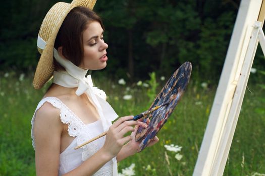 woman with a palette of paints painting a picture outdoors close-up. High quality photo