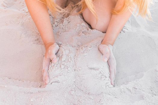 The hands of a young girl hold a pile of white sand close-up.