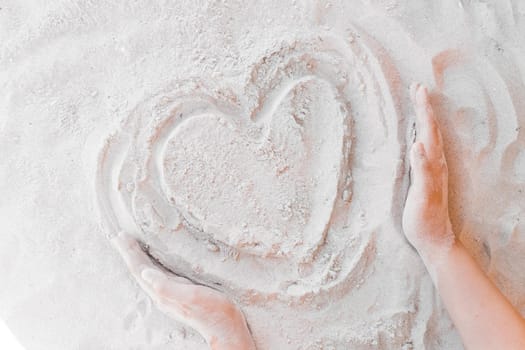 The hand of a young girl draws a heart on the white beach sand close-up. Symbol or sign of love concept.