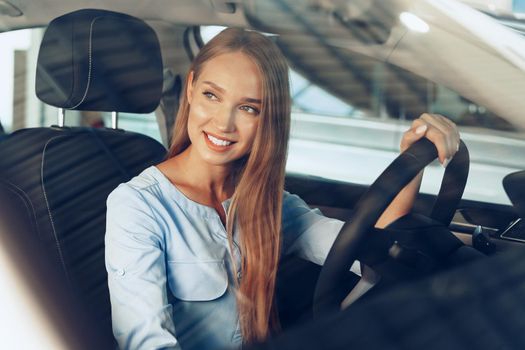Attractive young woman sitting in new car in showroom close up