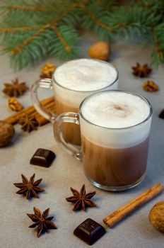 Hot Christmas Drink Cocoa Coffee or Chocolate with Milk Cream in a Small Transparent Cup. Fir Tree Branch, Nuts, Cinnamon Sticks Star Anise on a Grey Background. Winter time. New Year