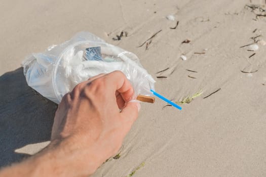 Man's hand picks up or collects garbage on a seaside beach close-up.