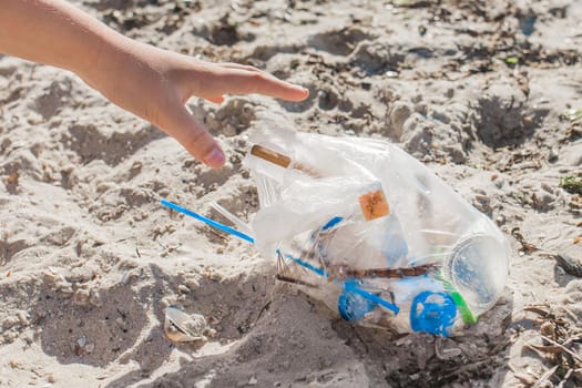 The girl's hand cleans up the garbage on the beach. Pollution and Ecology Concept.