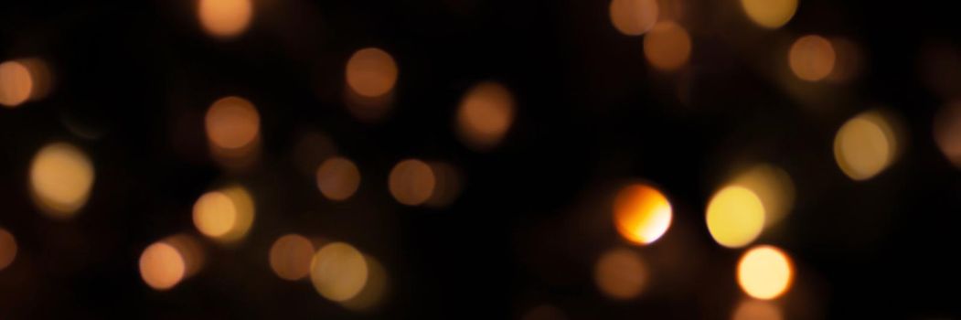 Banner of defocused bokeh lights on black background, an abstract naturally blurred backdrop for Christmas eve or birthday party. Festive light texture. Gold garland in blur. Overlay effect for design