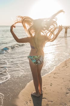 Young skinny girl throws up her hair and spreads her arms to the sides against the backdrop of the sea beach and sunset.